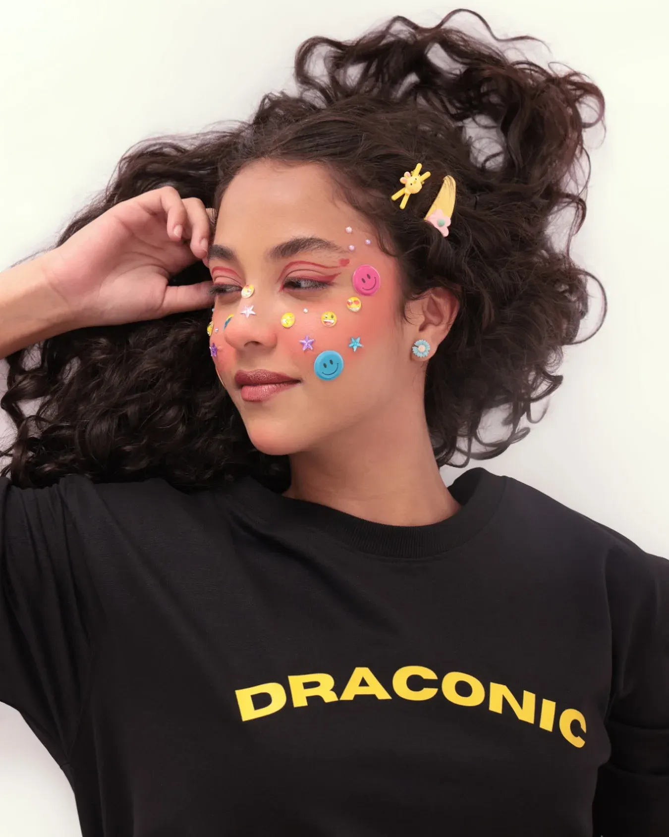 Model with star-shaped face gems wearing a black oversized Draconic tee