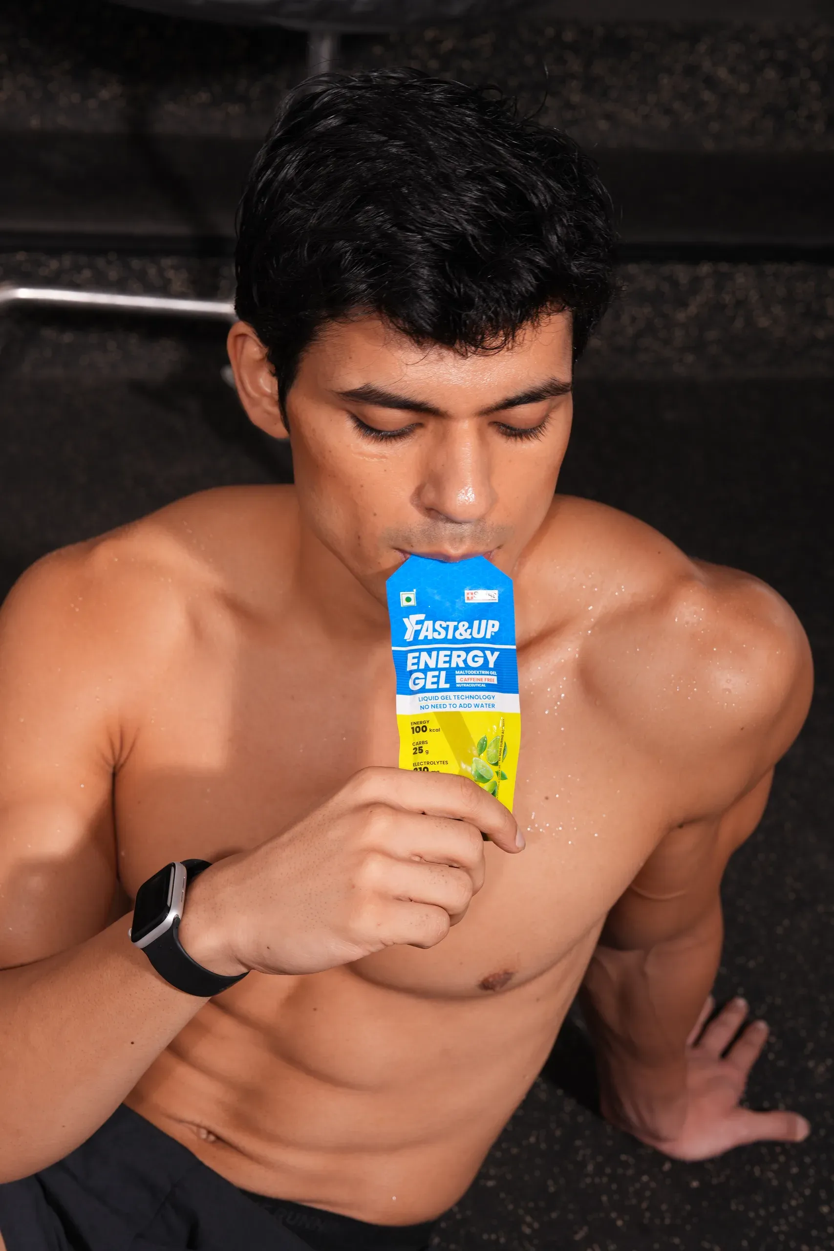 Shirtless athlete taking a Fast&Up energy gel in a dark gym studio