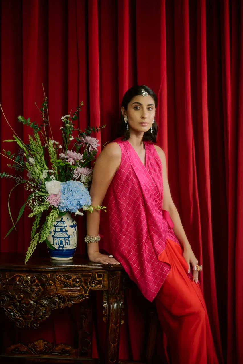 Model in a floral appliqué top and chartreuse skirt, seated on a carved sofa before red velvet curtains