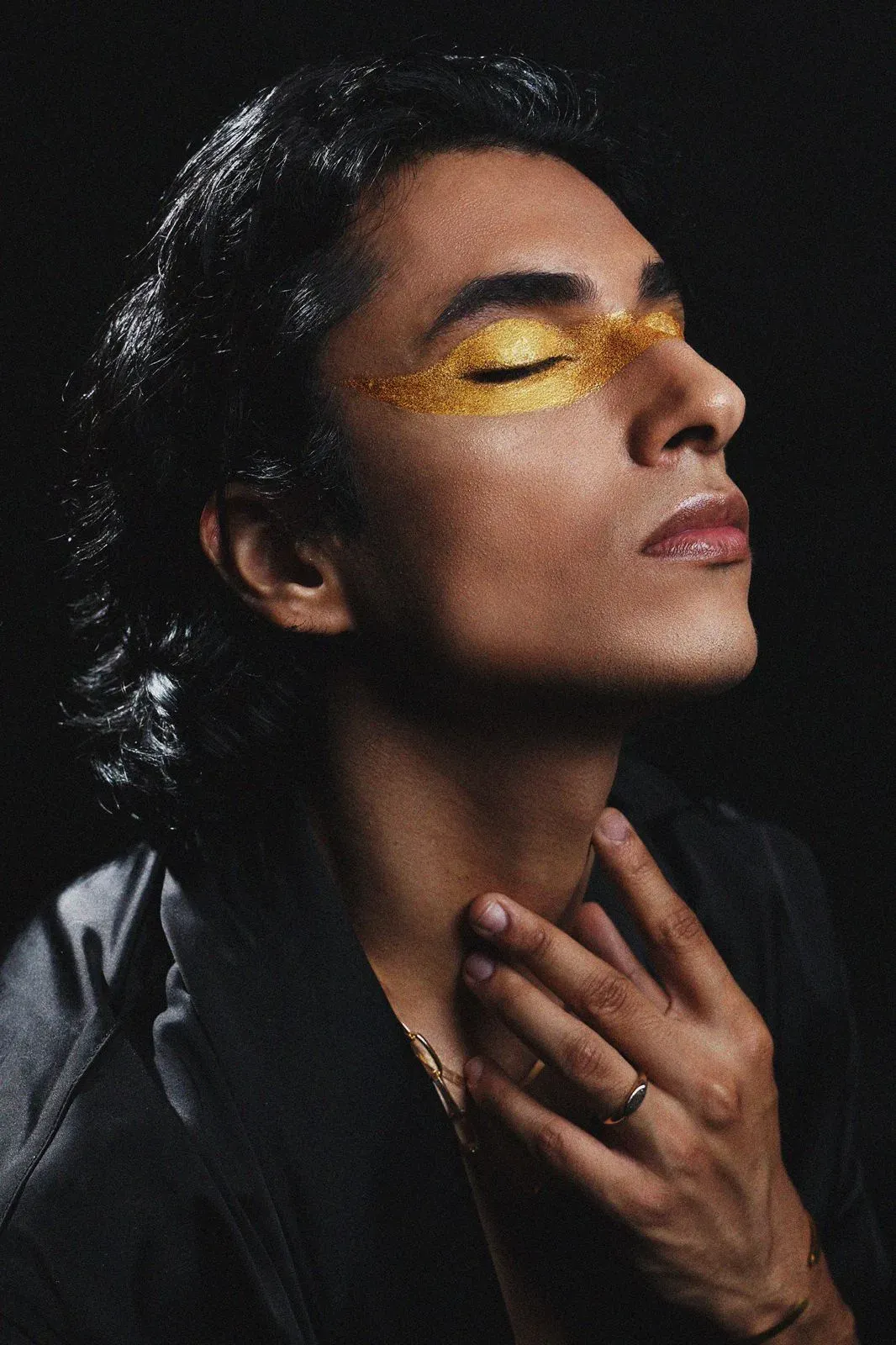 Beauty portrait of a model with gold pigment painted across the eyes, lit against black