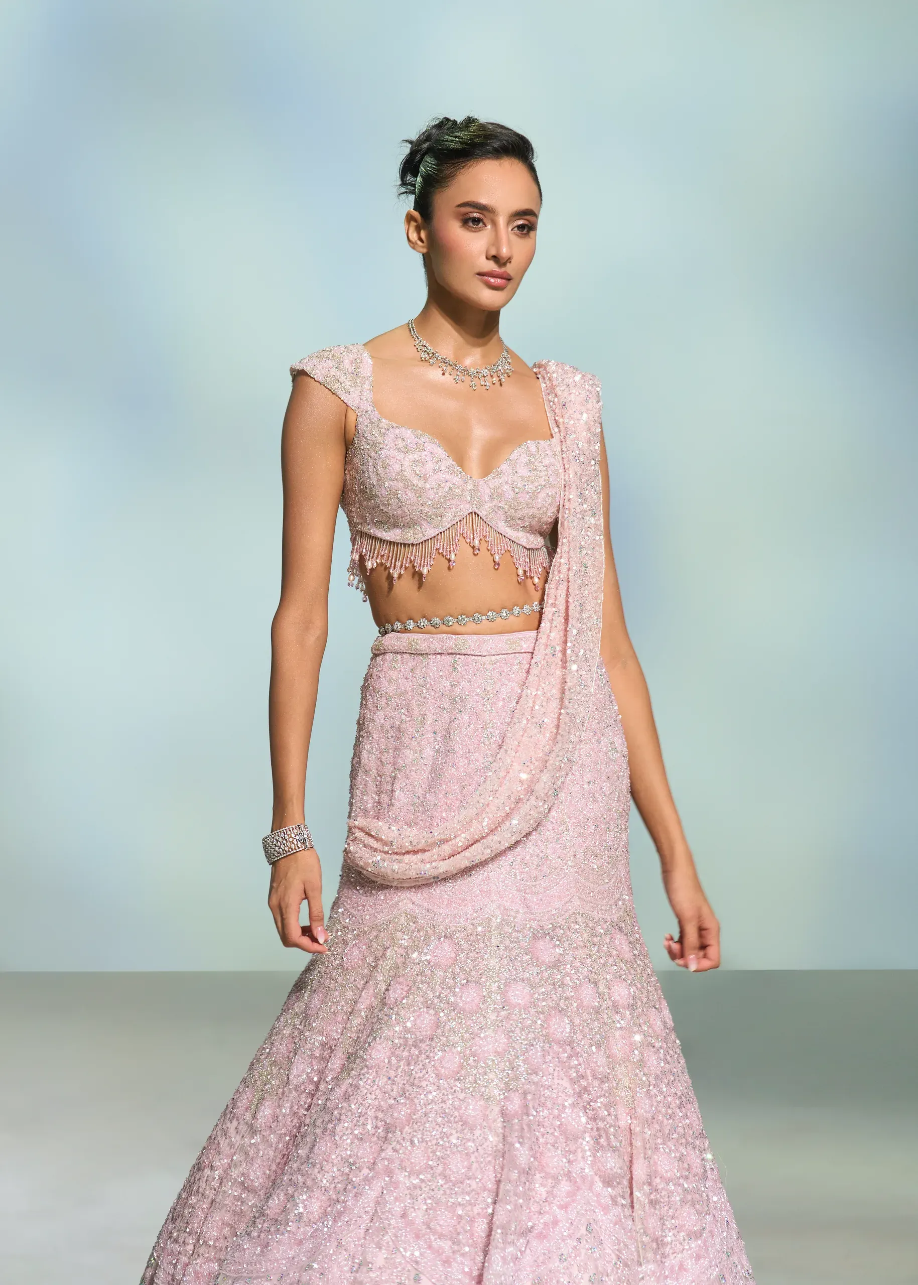 Model in a blush sequinned lehenga sari with a beaded blouse, against a pale blue-grey gradient